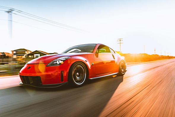 Red Nissan 350Z driving on a road at sunset